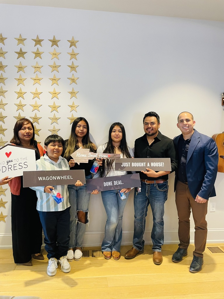Gustavo Hernández, su familia y Carlos Castro sostienen varios letreros de celebración por la compra de una vivienda.